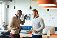 Cheerful Multiracial Businessmen High-fiving While Standing In Creative Office