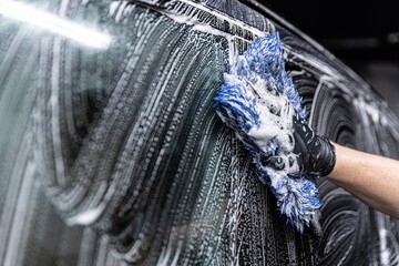 Wall Mural - car wash employee thoroughly washes a modern car with a dedicated washing mitt