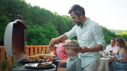 Wall Mural - Man grilling ribs and vegetable on grill during family summer garden party, close-up