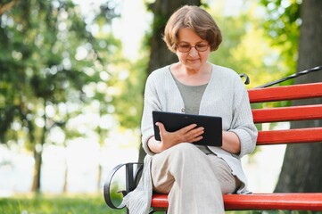 Sticker - Elegant elderly woman in the shirt is sitting on the bench in a park on a warm day