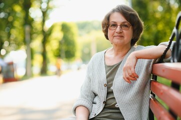 Wall Mural - Elderly woman sitting and relaxing on a bench outdoors in park