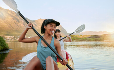 two smiling friends kayaking on a lake together during summer break. smiling and happy playful women