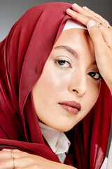 Wall Mural - Portrait of an elegant muslim woman in a hijab posing in a studio. Headshot of a stylish, classy confident arab model standing against a grey background. Fashionable woman wearing a headscarf