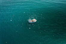 Aerial View Of Fishing Boat In Turquoise Sea Pulling In Lobster & Crab Pots While Seagulls Fly Overhead, Mevagissey, Cornwall, United Kingdom.