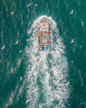 Aerial View Of Fishing Boat In Turquoise Sea Pulling In Lobster & Crab Pots While Seagulls Fly Overhead, Mevagissey, Cornwall, United Kingdom.