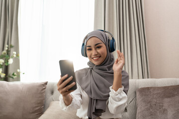 Wall Mural - Muslim woman sitting on sofa and video conference calling on mobile phone. Muslim asian woman video call.