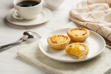 Traditional portuguese vanilla pudding puff pastry pastel de nata on white plate on marble board with a cup of coffee in white porcelain