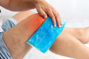 man using cool gel pack on a swollen injured knee with color enhanced skin with red spot indicating 