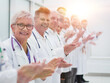 © ASDF - smiling female doctor standing in front of her applauding colleagues.