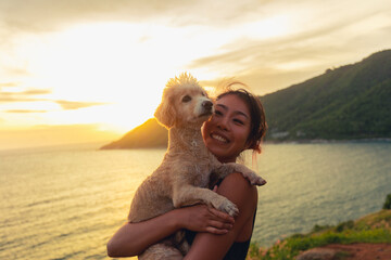 Candid Asian woman hugging dog happy on the beach at travel and vacation. Female Happy smile with pet as new life at sunset. life balance concept