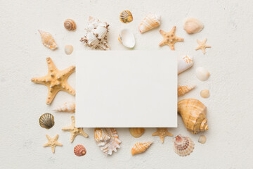 Summer time concept with blank greeting card and blank white paper on colored background. Seashells from ocean shore in the shape of frame separated with space for text top view