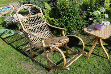 Rocking chair for recreation from rattan and small wicker table in summer garden on lawn in summer on sunny day