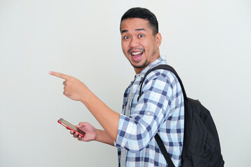 Side view of Adult Asian man wearing backpack and holding handphone with excited expression