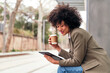 © Raul Mellado - happy latin woman using her tablet and drinking coffee while waiting for the bus, concept of urban life style