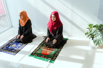 Two young Asian Muslim women in hijab dress sitting and praying together. Idea for religious ritual, education and calm of mind