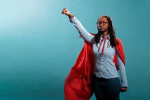 Proud And Strong African American Justice Defender Looking Ambitious While Looking At Camera. Powerful And Brave Young Superhero Woman Wearing Hero Costume While Posing As Flying On Blue Background.