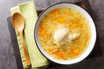 Delicious homemade chicken broth with noodles and vegetables close-up in a plate on a wooden tray. horizontal top view from above