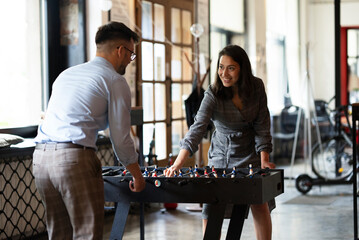 Colleagues having fun at work. Businessman and businesswoman playing table soccer..