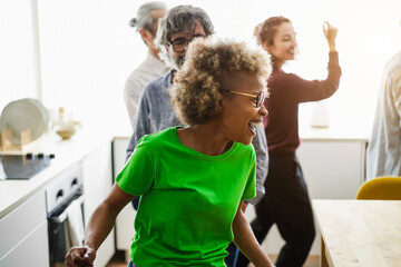 Multi-generational friends having fun dancing at home kitchen - Soft focus on african woman face