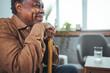 © Dragana Gordic - Portrait of a senior man sitting at home with a walking stick. Senior Afro-American with Walking Stick is Sitting in Comfortable Armchair in the Living Room at Home.