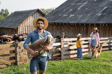 Wall Mural - happy farmer with lamb looking at camera near family and cattle dog on farm.