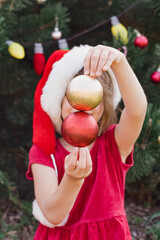 Wall Mural - Merry Christmas. Portrait of happy funny child girls in Santa hat with Christmas tree toys near face. No face. Happy Holidays. Fairy Magic. Happy kid enjoying holiday. Christmas in July