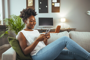 Wall Mural - Cropped shot of an attractive young woman using her cellphone while sitting in the living room during the day. Shot of a young woman using a cellphone while relaxing on a sofa at home