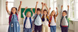 Small team of children having fun at school. Group portrait of happy classmates with backpacks standing in row in the classroom, smiling, raising arms and shouting Yay, Hooray. Back to school concept