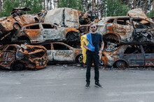 Man With Ukrainian Flag Stands Against Cars Cemetery In Irpin. Consequences Of The Russian Military Invasion In Ukraine.