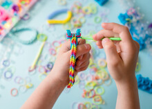 A Girl Makes A Rainbow Bracelet From Rubber Bands Crochet. Closeup Of Making Decorative Bracelet With Elastic Bands. Loom Bracelets