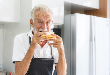 An elderly Caucasian man wearing an apron Eating homemade sandwich bread