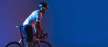 One Male Cyclist Riding Bicycle Wearing Cycling Shorts And Protective Helmet Isolated On Dark Blue Background In Neon. Concept Of Sport, Speed, Energy