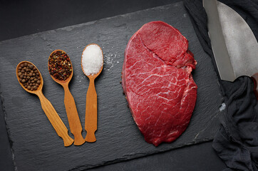 Wall Mural - Raw beef tenderloin lies on a wooden cutting board on a black table, top view