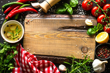 Wall Mural - Food background. Oak cutting board, spices and vegetables at dark kitchen table. Top view with space for design.