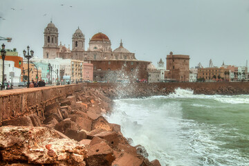 Cadiz, Spain - December 21, 2019: Dramatic urban landscape with the cathedral of Cadiz next to a rough sea