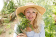 © Girts - Mature blonde woman holding fresh greens from home garden. Spring vitamin at community greenhouse. Woman holding dills. Sunny day in yard with greenery. Picking vegetables in local gardens.