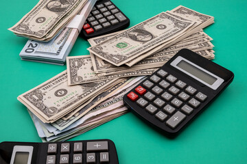 Close-up of a pile of dollar bills, surrounded by black calculators, on a green table. Concept of financial calculations.