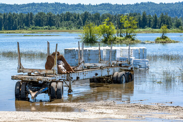 Sunken old rusty semi trailer and an unloaded stacked cargo standing in water after a Columbia River flood causes environmental damage in a recreational area of a national reserve