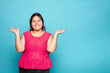 © Lux Images - Young curvy Latina woman smiling and presenting copy space for product with both hands open, isolated on blue background.