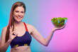 Smiling sporty woman in sportswear green salad in glass bowl and ok showing. Female fitness portrait isolated on neon multicolor background.