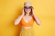 © sementsova321 - Image of smiling happy positive woman wearing top and panama, posing with raised arms and looking at camera with positive happy expression, standing against yellow wall.