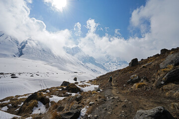 Rocky trail pathway with natural landscape view of snowcapped mountain range with cloudy blue sky- Himalayas ridge, Nepal