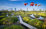 Fototapeta  - Hot air balloons floating up to the sky over big green forest park in morning, Benchakitti Forest Park in Bangkok, Thailand.