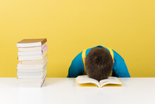 Stressed Boy Sleeping With Head On Table.  Overwhelmed Student Isolated On Yellow Background.