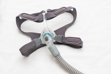 CPAP mask and headgear connection to a CPAP hose on white bed sheet