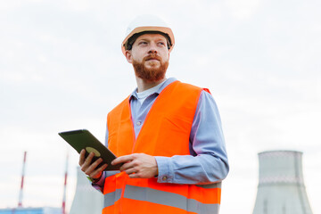 A successful professional. The man is an engineer in a helmet and a protective orange vest. Tablet in hand