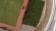 A dynamic rotating aerial footage of a group of students lying on the grass of the athletic stadium while doing exercises and arm movements.