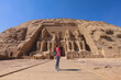 © Dave - White Woman Tourist in front of the Colossal Statues of Ramesses II seated on a throne near the entrance to the Great Temple at Abu Simbel, Egypt