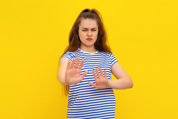 Wall Mural - Image of brunette girl express disgust or dislike, grimacing from aversion, refusing, rejecting smth bad, standing in white-blue striped t shirt over yellow background. Body language concept