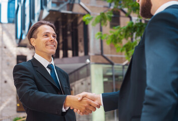 Wall Mural - Confident businessman and his colleague in front of modern office building. Financial investors in formal wear are talking outdoor. Banking and business.